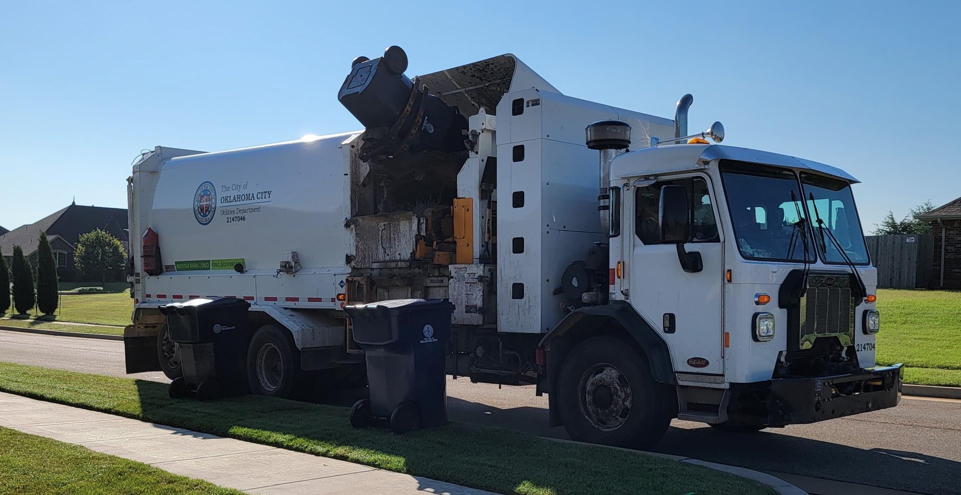 A Utilities solid waste truck picking up trash in a neighorhood.