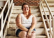 person with long hair and white tank top smiling and sitting on outside stairwell