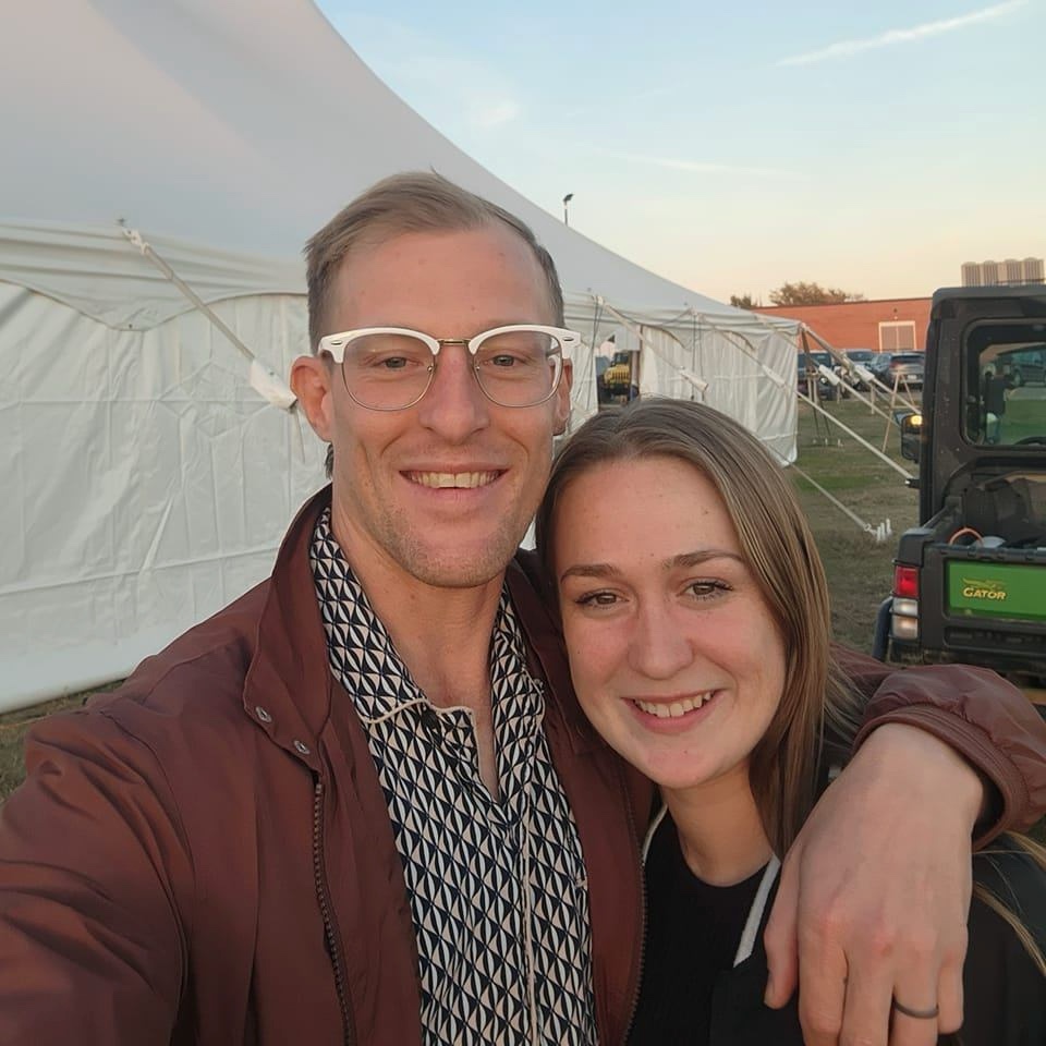 man and woman smiling at the camera in front of white tent